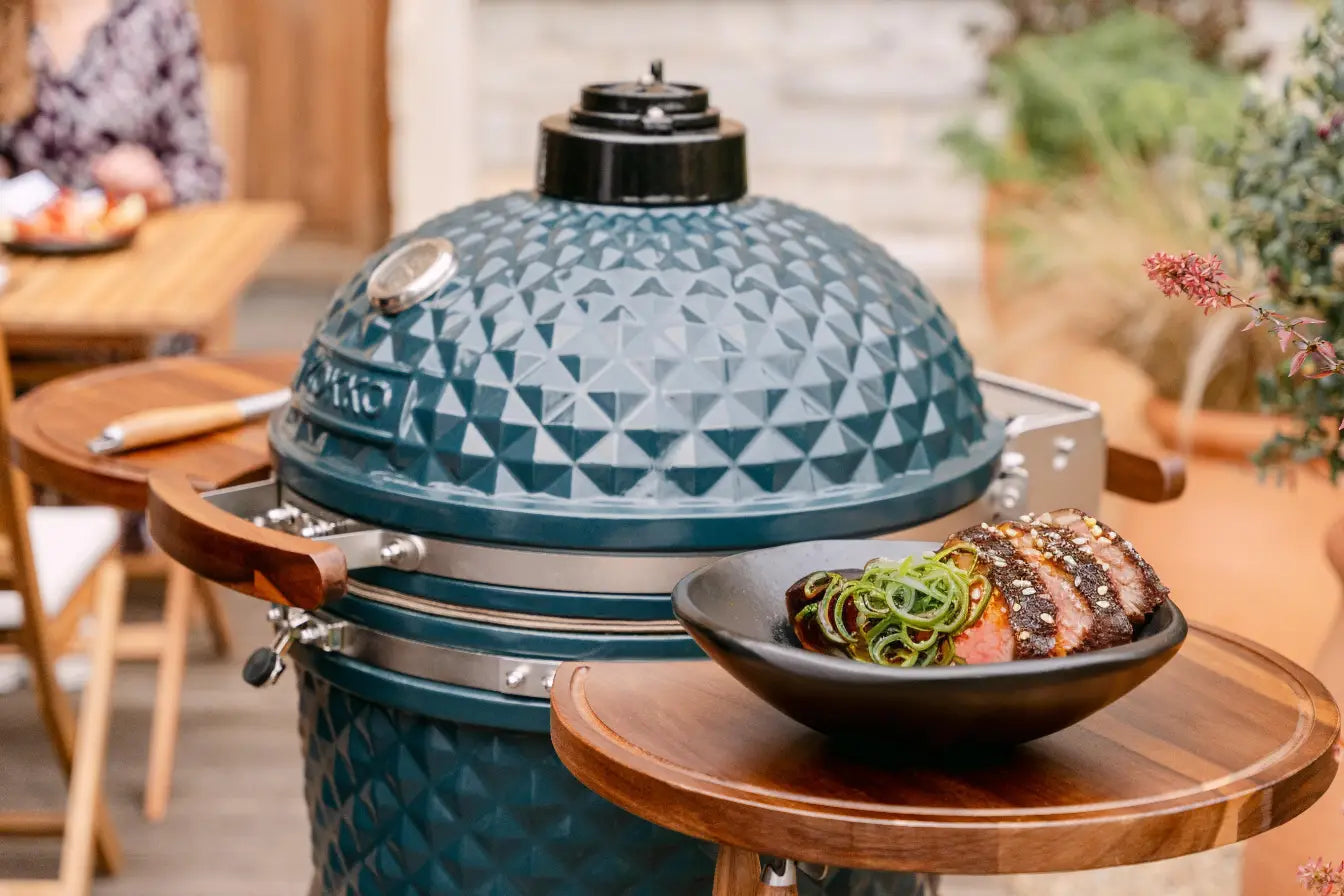 Kamado avec un plat de tataki de bœuf servi, enrobé de graines de sésame blanc et noir, herbes fraîches, et accompagné d'une sauce à base de soja, gingembre et miel pour une touche finale savoureuse.