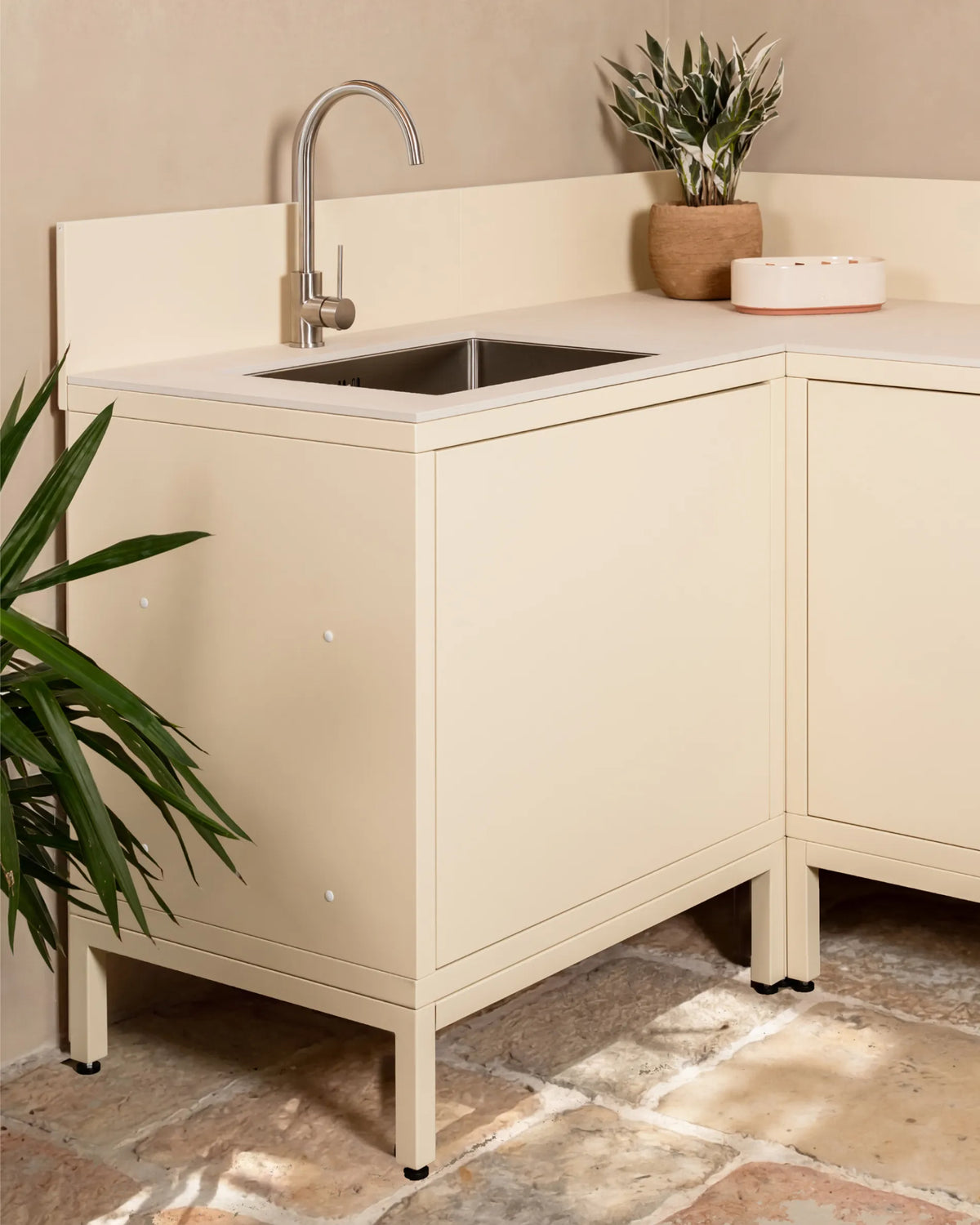 Cream beige PILOTIS base structure under corner sink unit, outdoor kitchen with faucet and plant