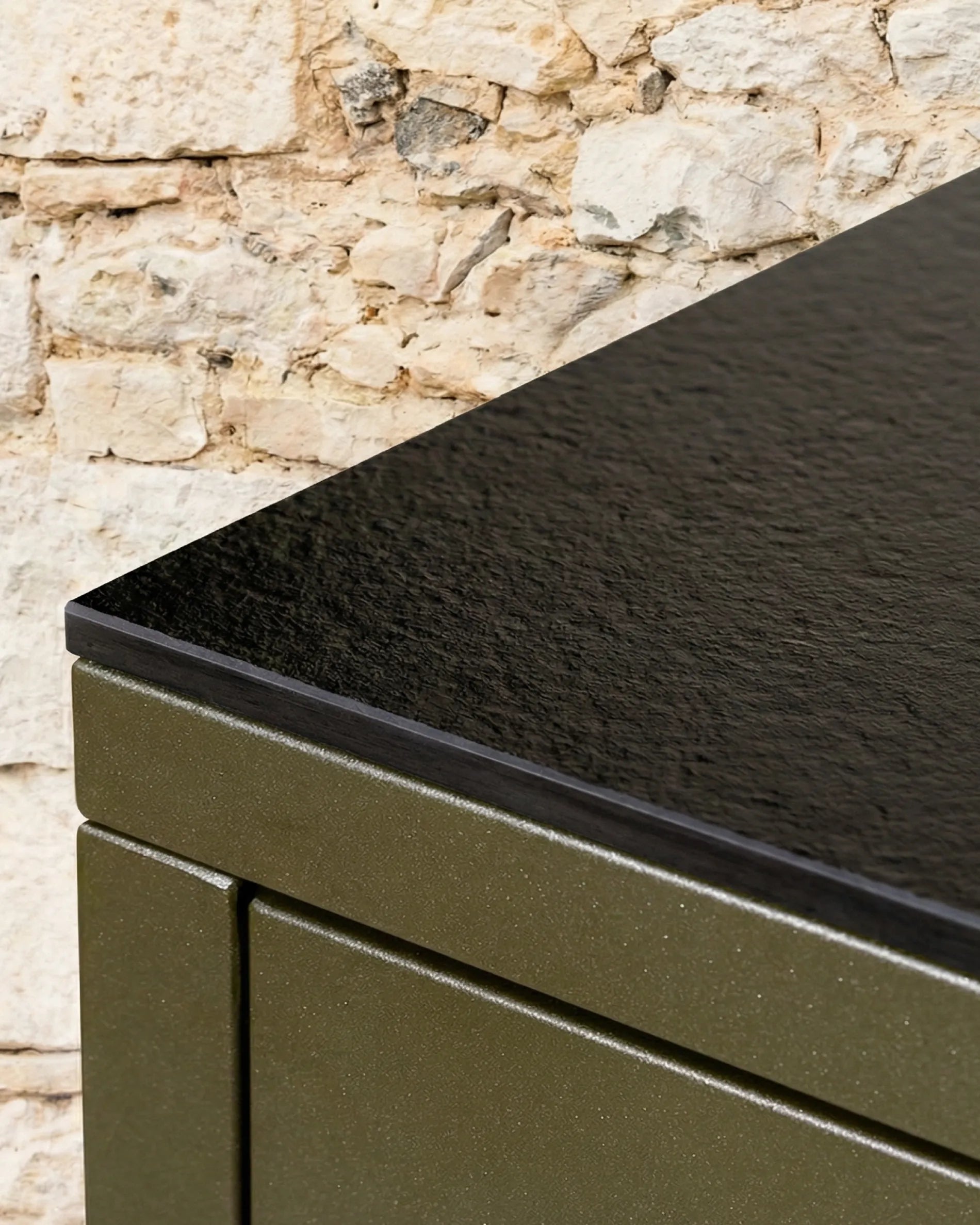 Close-up of the black PILOTIS tabletop corner joint, with the olive green unit against a stone wall
