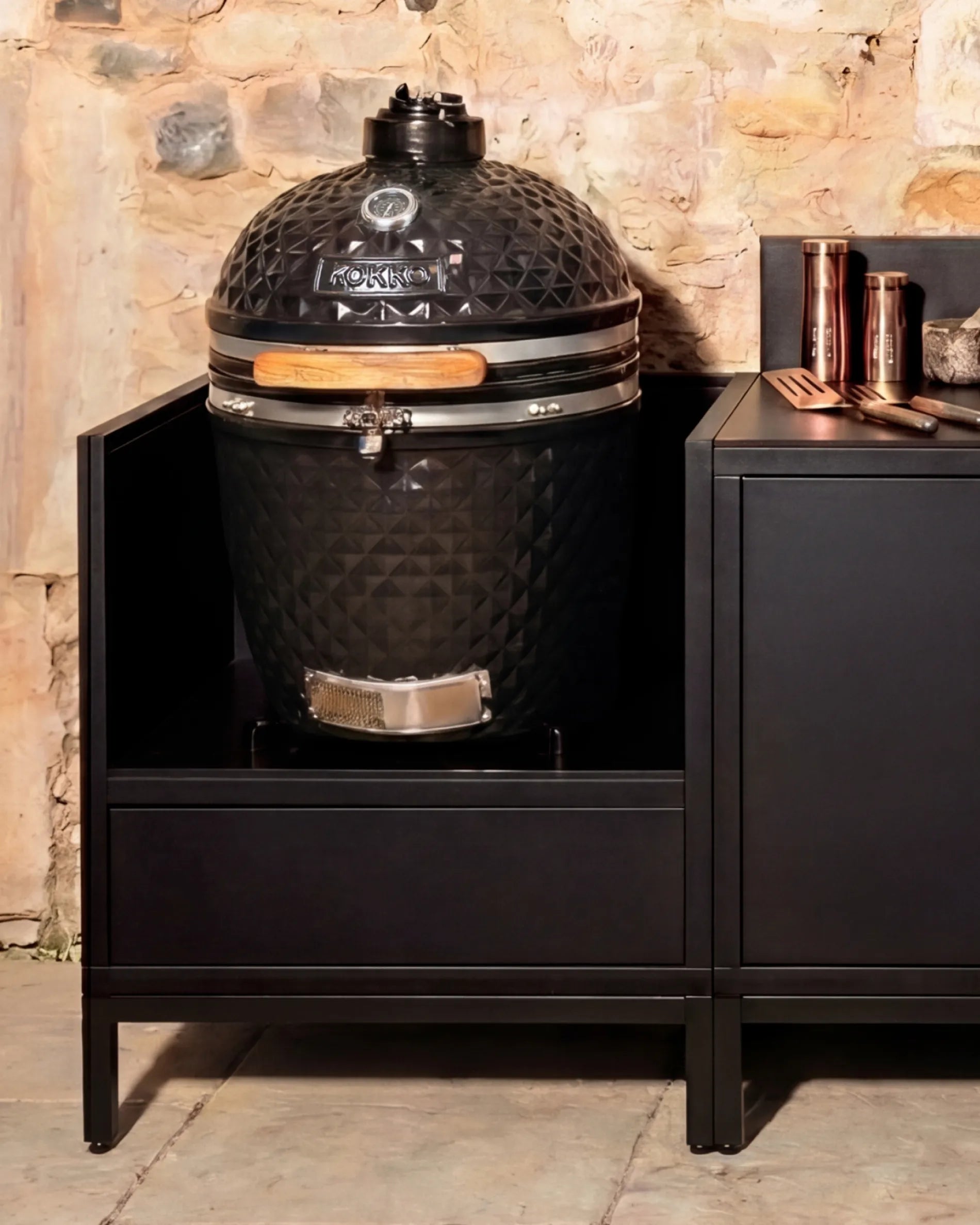 Black Kokko kamado barbecue installed in a PILOTIS enclosure with copper accessories, outdoor kitchen