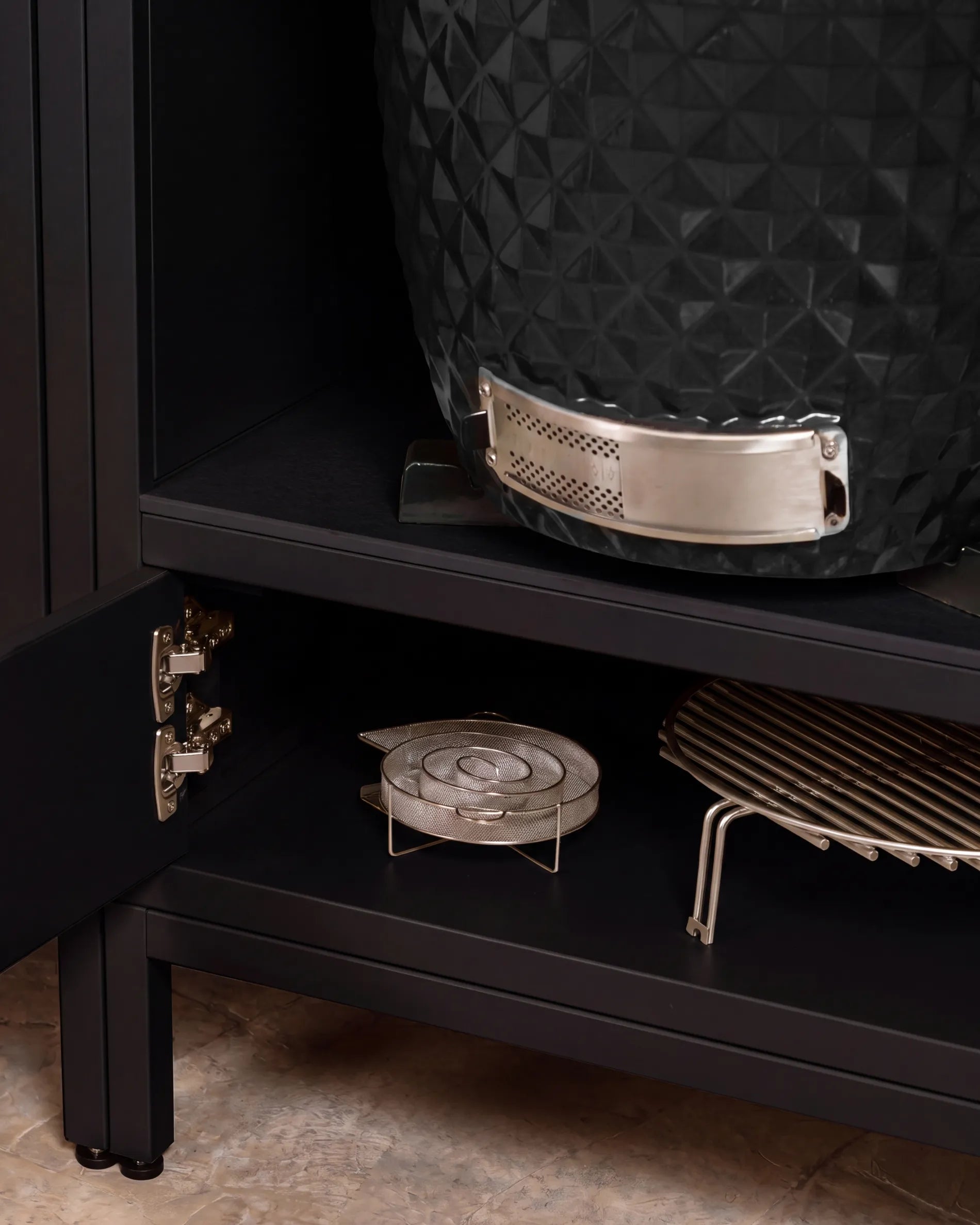 Black Kokko kamado barbecue in the PILOTIS unit niche, close-up on the hinge and storage racks