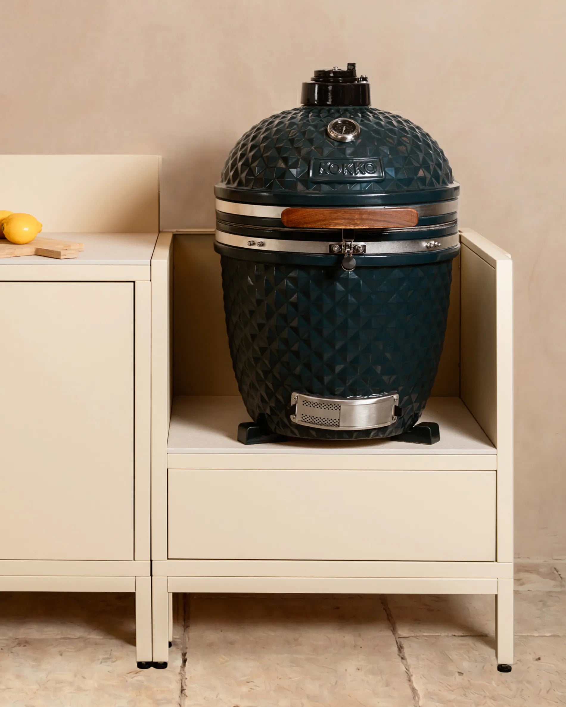 Navy blue Kokko kamado barbecue installed in a cream beige PILOTIS enclosure, outdoor kitchen
