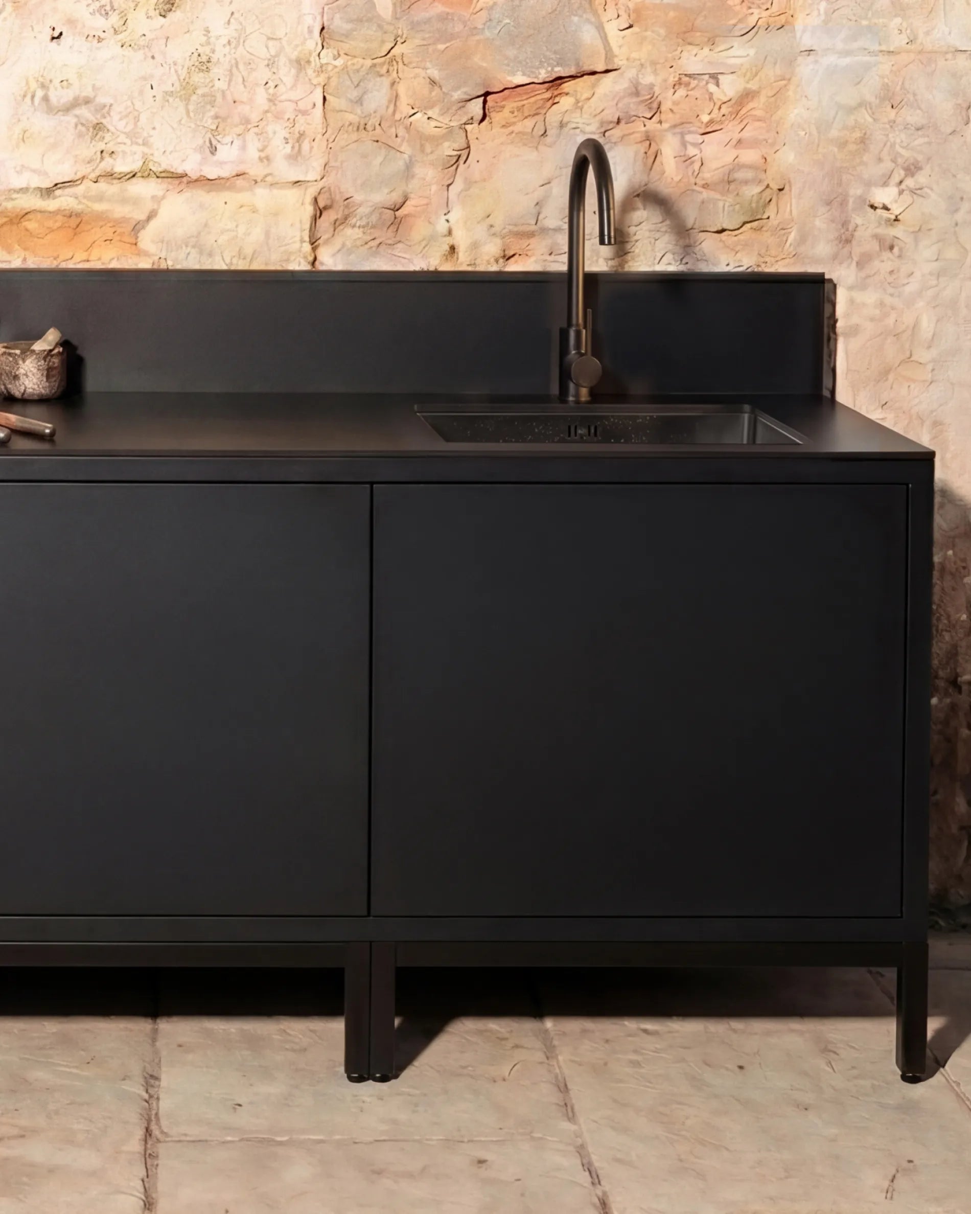 Black corner unit PILOTIS Sink Module with faucet, outdoor kitchen against a stone wall