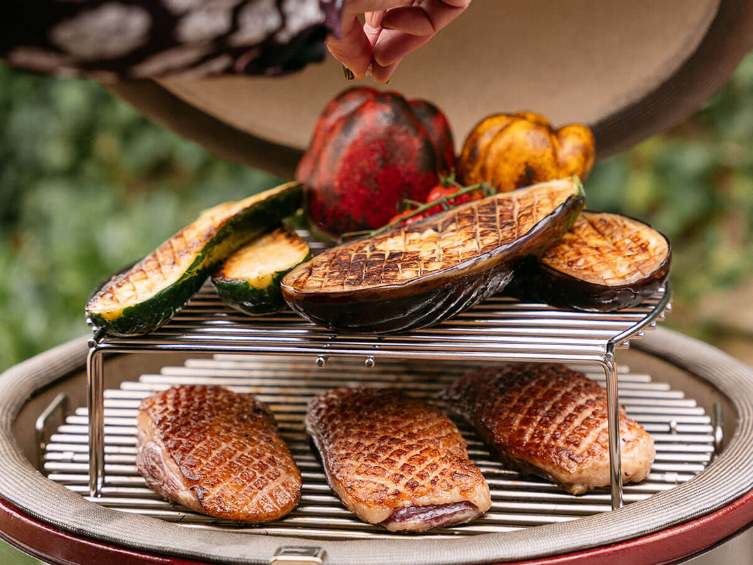 Two-level cooking in a Kokko kamado with duck breasts seared on the lower grate and vegetables grilled on the elevated rack, showcasing versatile cooking.