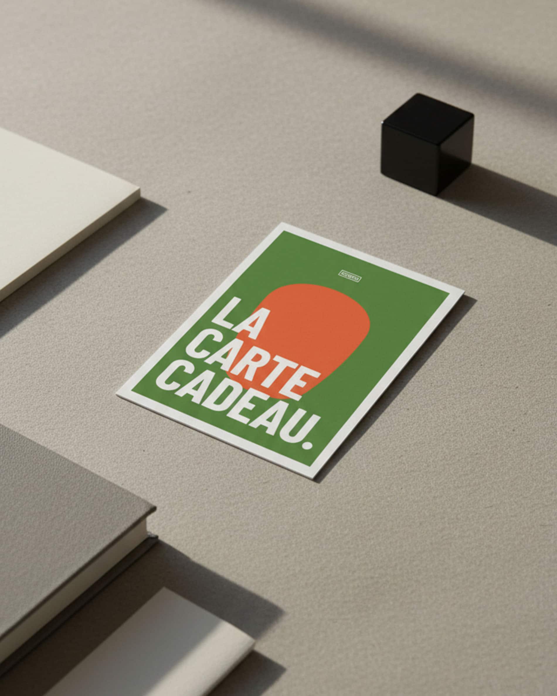 Carte cadeau kokko posée sur une surface minérale, visuel graphique vert et orange avec texte « la carte cadeau ».