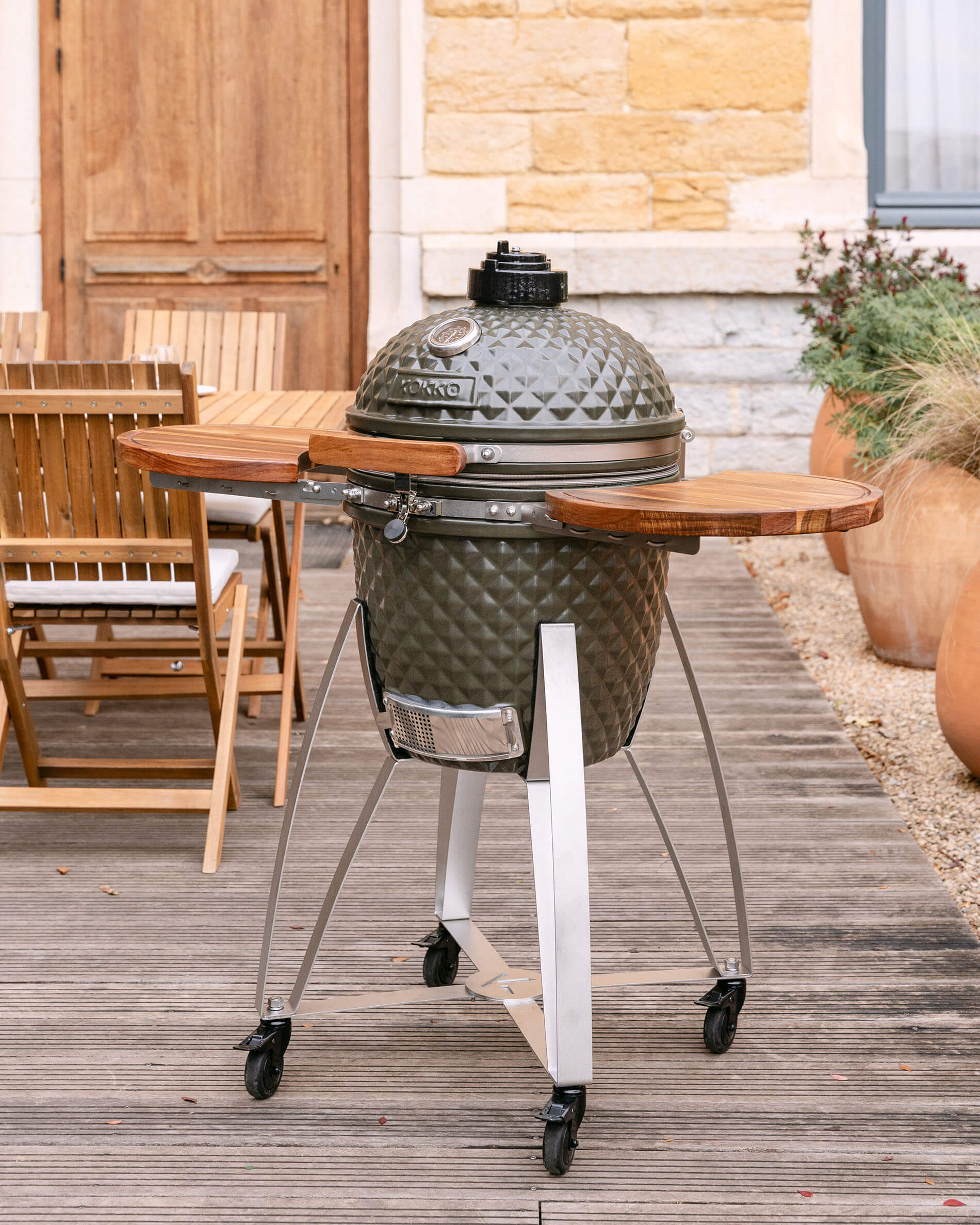 Kamado Kokko on a mobile cart with wooden side shelves, shown outdoors on a terrace.