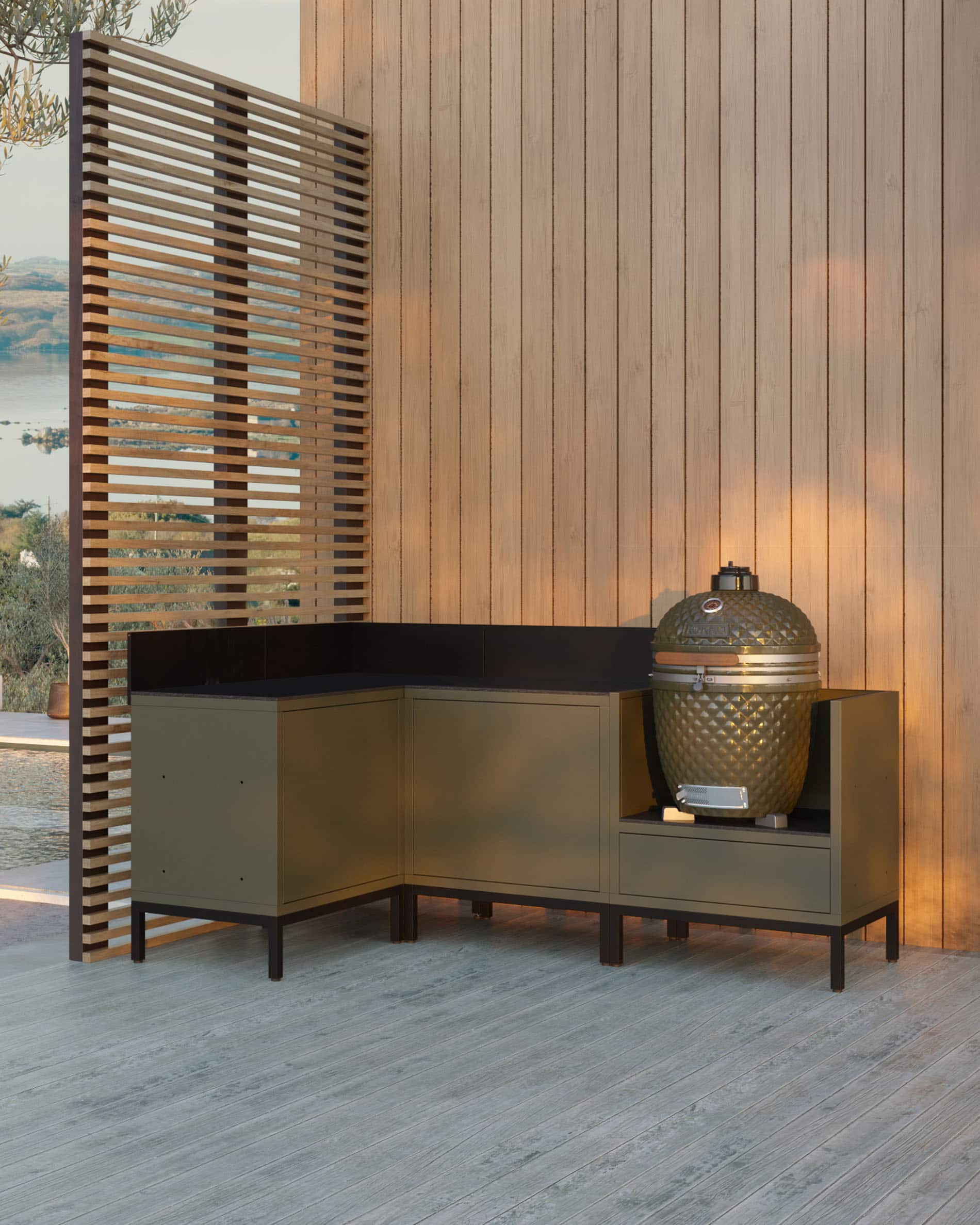 Module de cuisine pilotis d’angle pour kamado, ensemble de meubles coloris vert olive avec évier intégré, plan de travail sombre et crédence assortie, kamado installé dans le module latéral droit, structure sur pieds noirs.