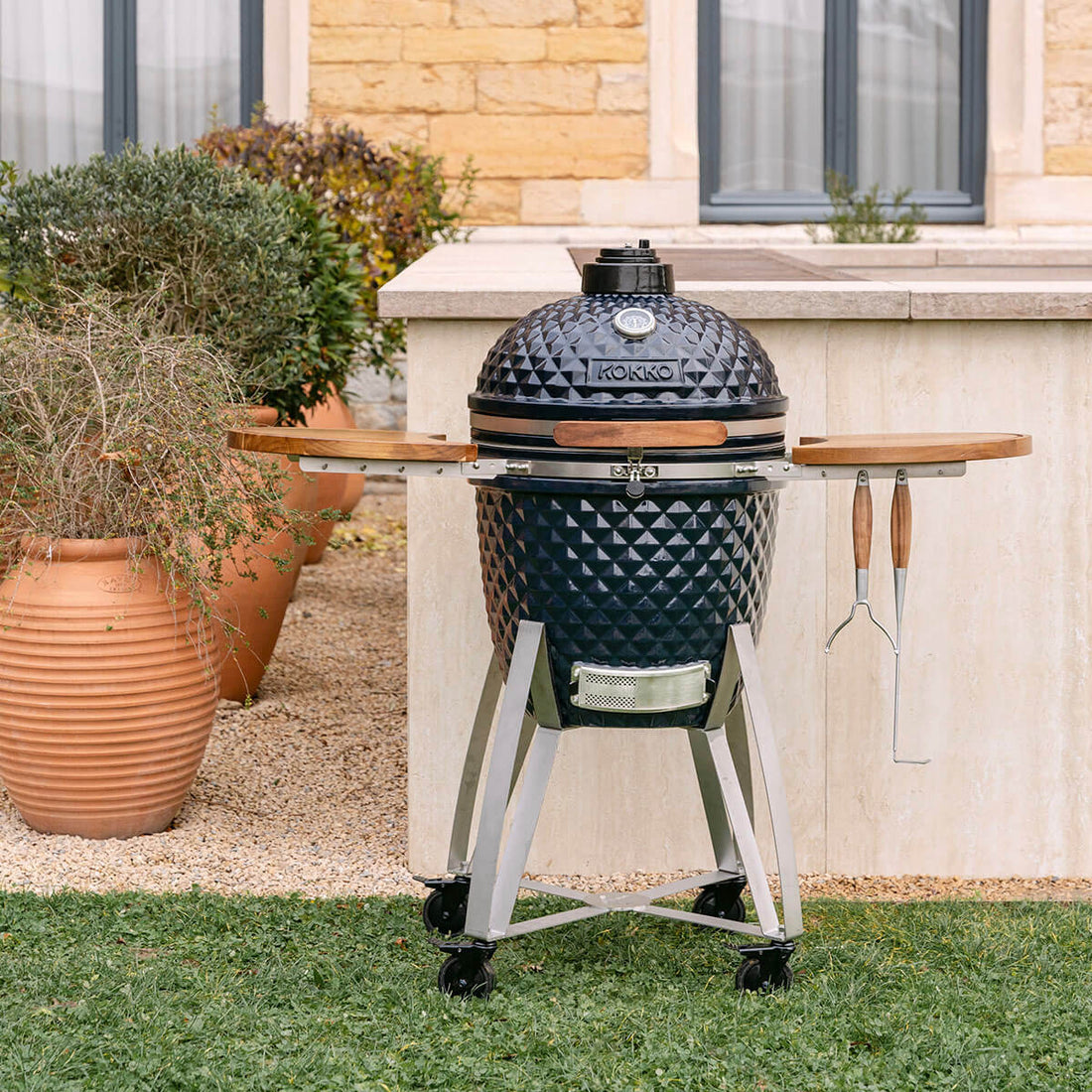 Kamado Kokko navy en céramique, équipé de tablettes en bois et d’un support mobile avec roulettes.