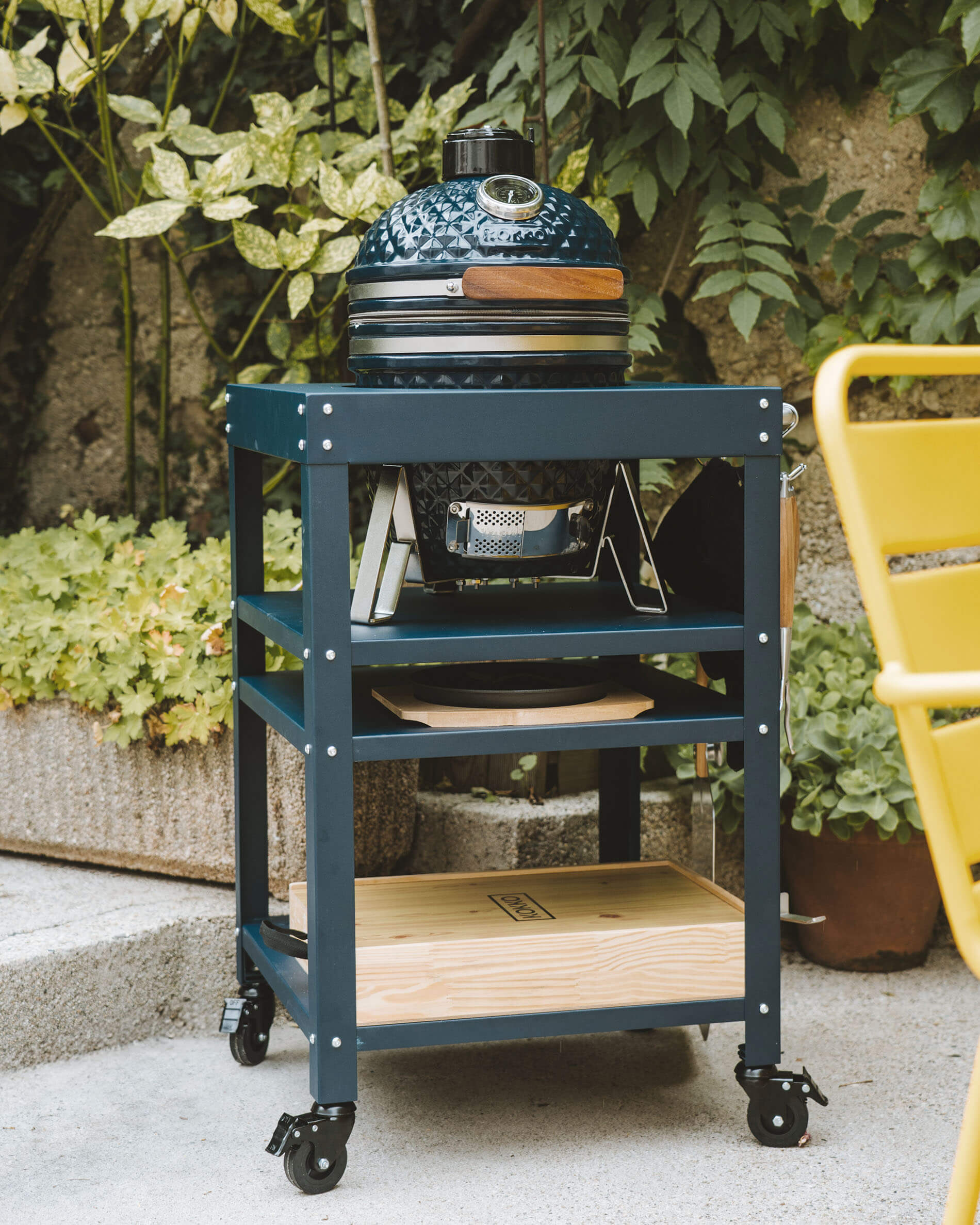 Overview of a Kokko Ocean Blue kamado set on a metal trolley with wheels, featuring utensil hooks and built-in storage spaces.