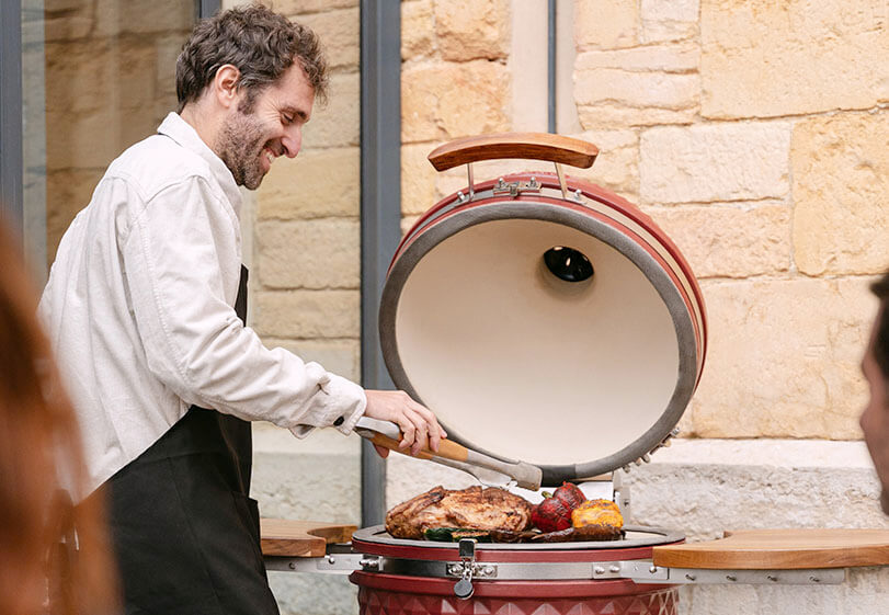 Kokko expert using an oxide red kamado outdoors to demonstrate best grilling practices.