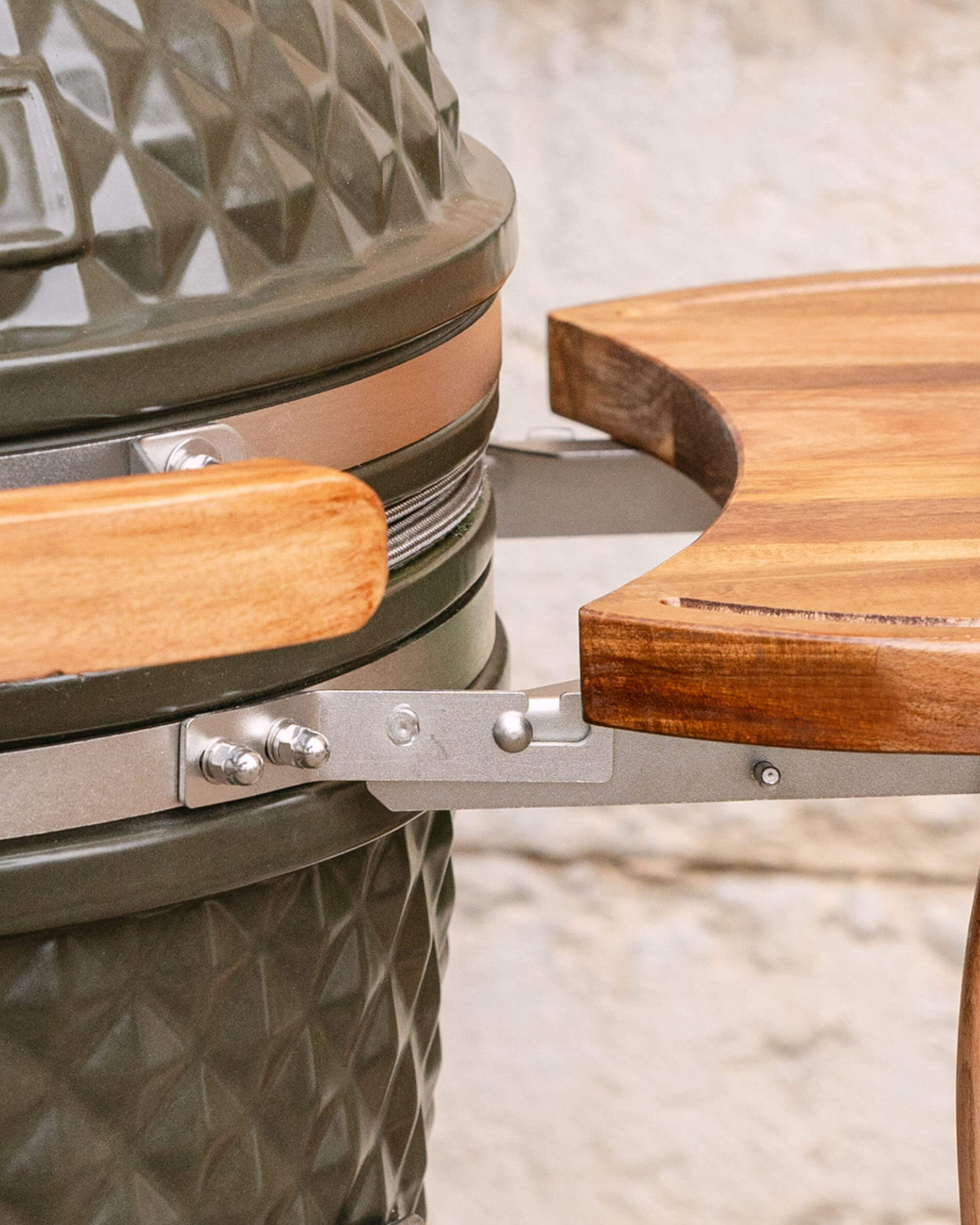 Close-up of the metal bracket connecting the wooden side shelf to the kamado, highlighting the attachment system and screws.