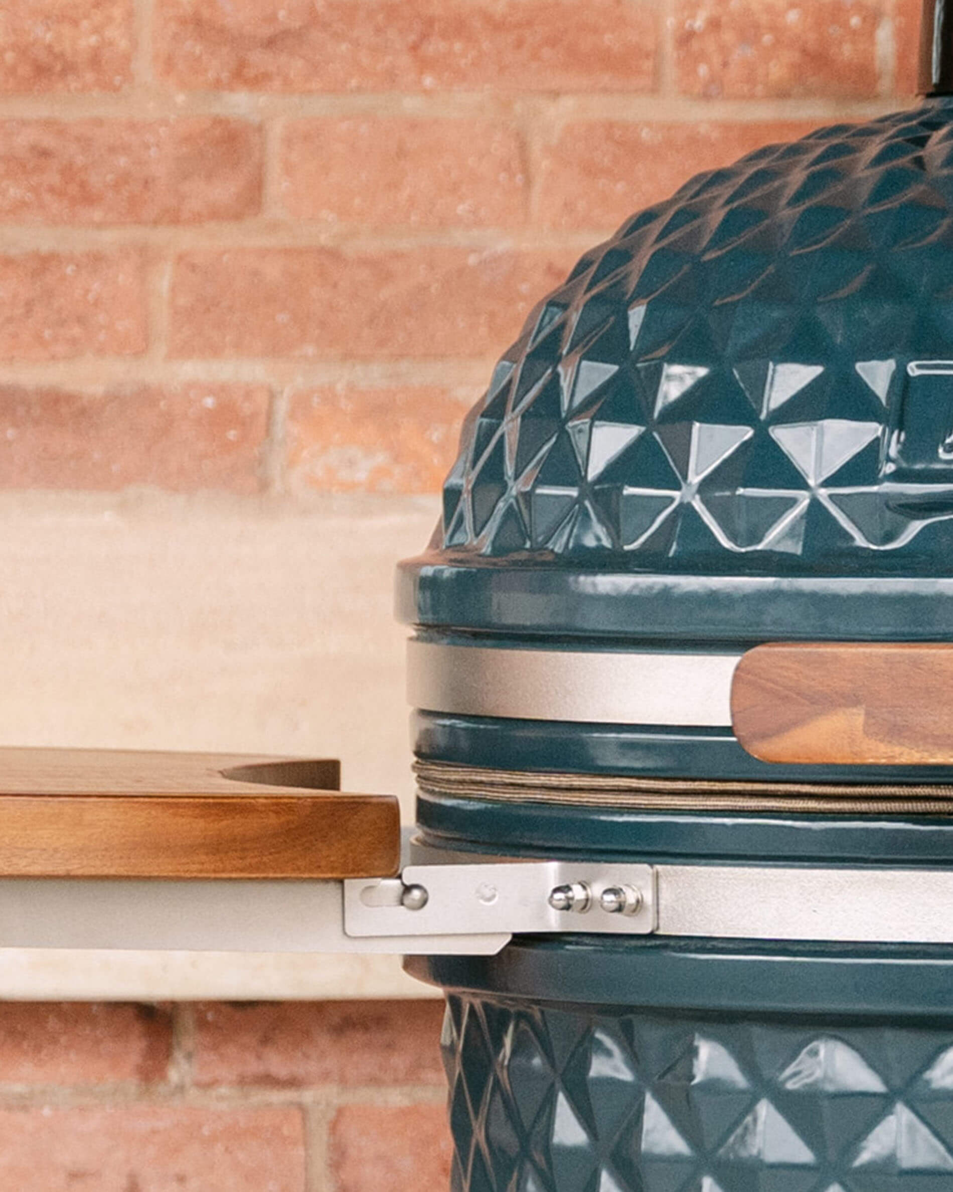 Close-up of the side mounting of a wooden shelf on a Kokko kamado, showing the metal support system connecting the shelf to the ceramic body.