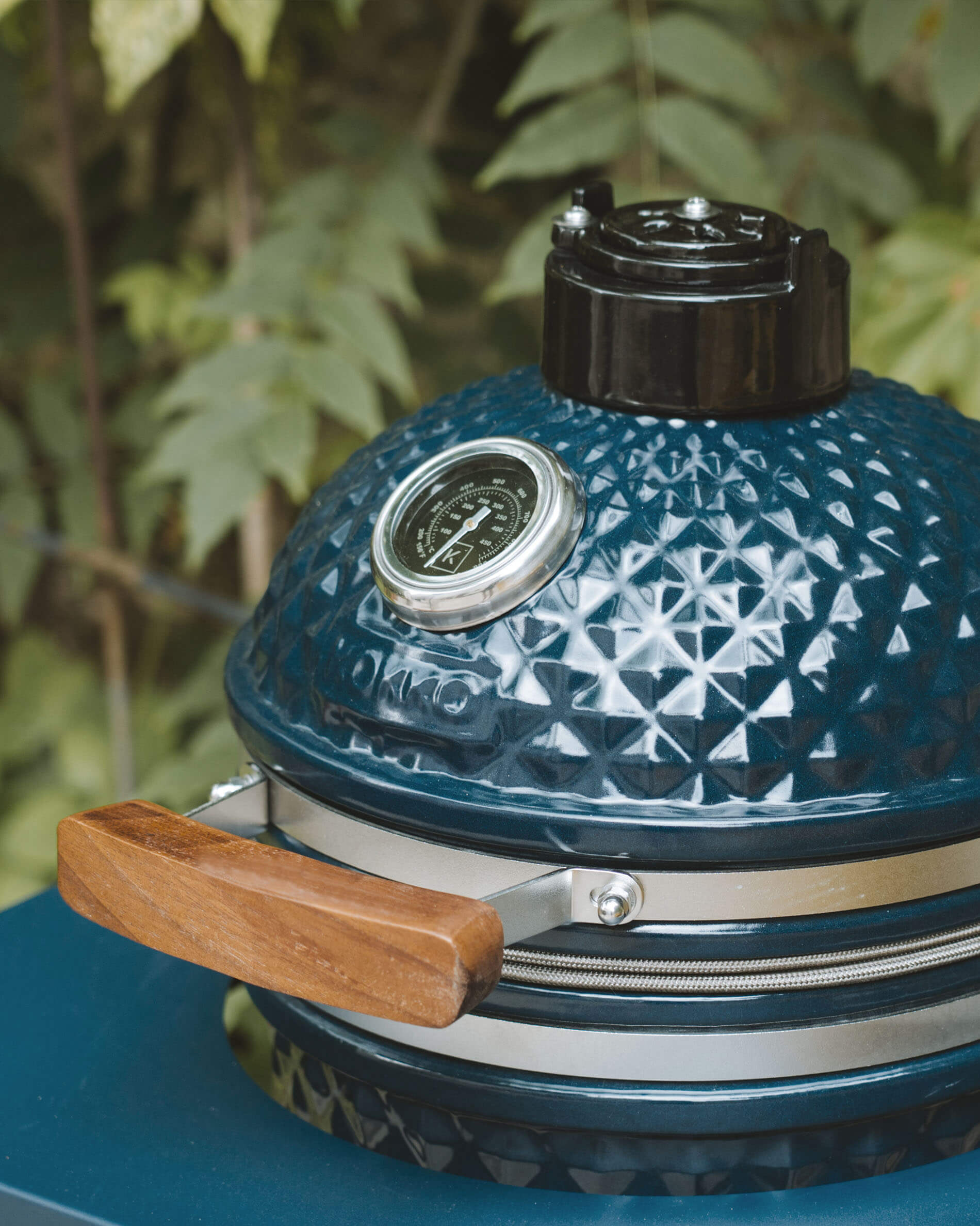 Détail du couvercle d’un kamado Kokko coloris océan avec thermomètre intégré et poignée en bois.