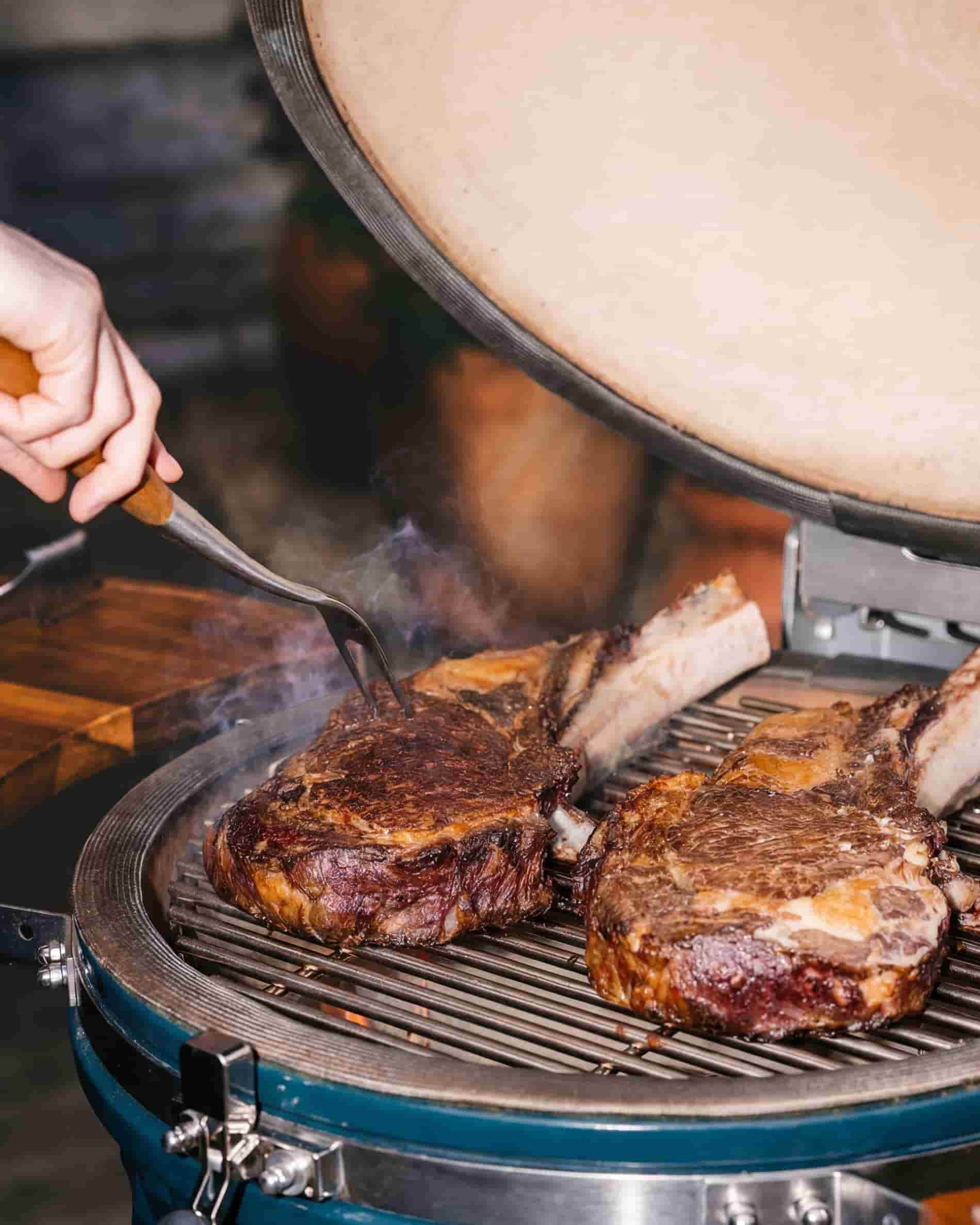 Grilling meat on the grate of a Kokko XL 22-inch kamado, lid open.