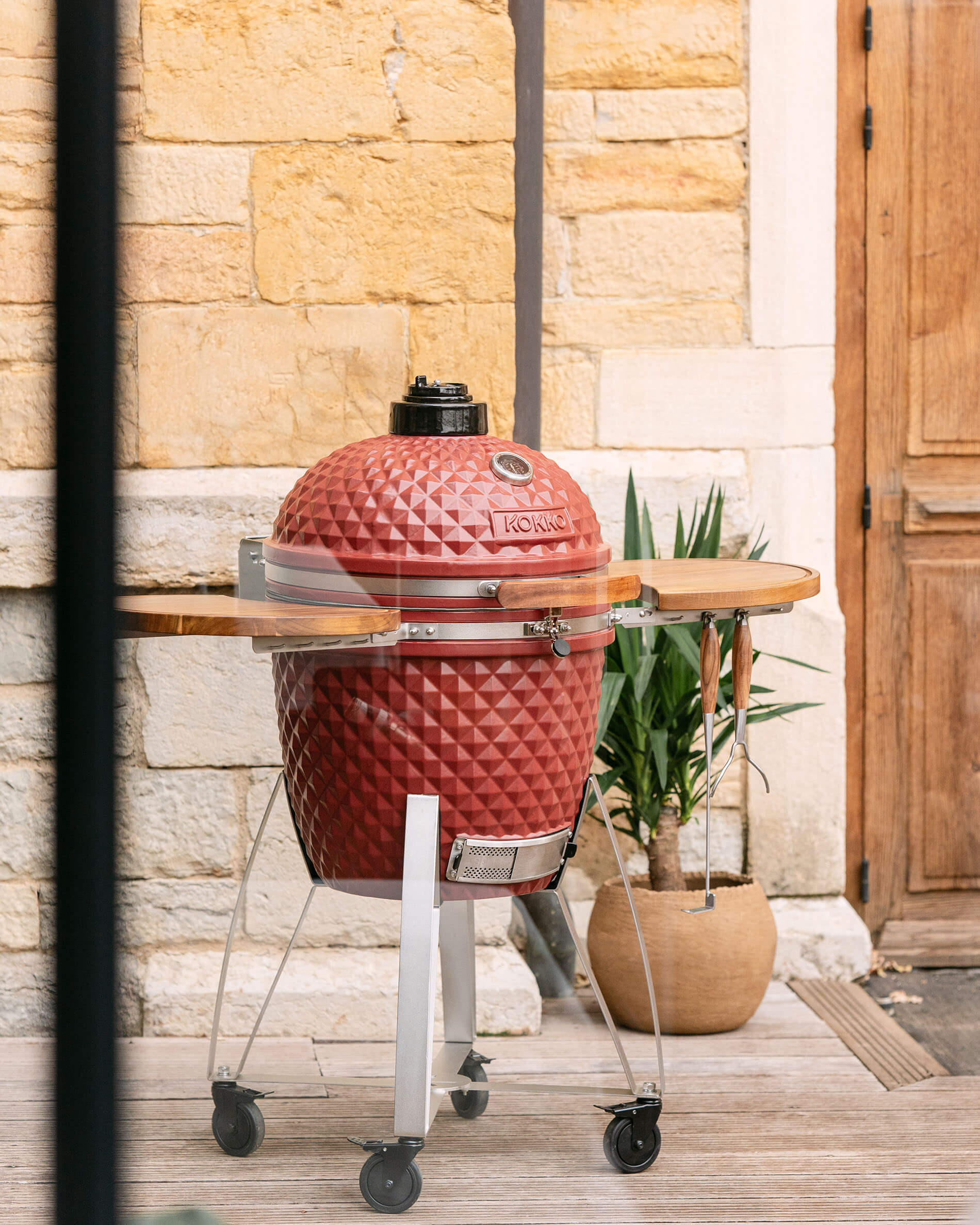 Kokko XL 22-inch ceramic kamado in oxide red, set on a cart outdoors.