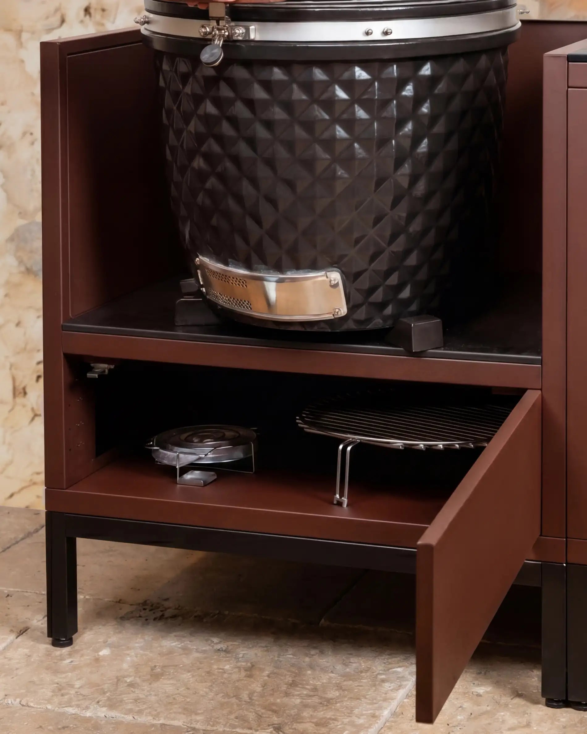 Black Kokko kamado built into a rust module with open storage shelf and cooking accessories