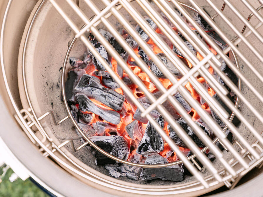 Glowing charcoal inside the ceramic bowl of a Kokko kamado, with red embers visible beneath the stainless steel grate, illustrating rising heat and precise wood-fired cooking control.