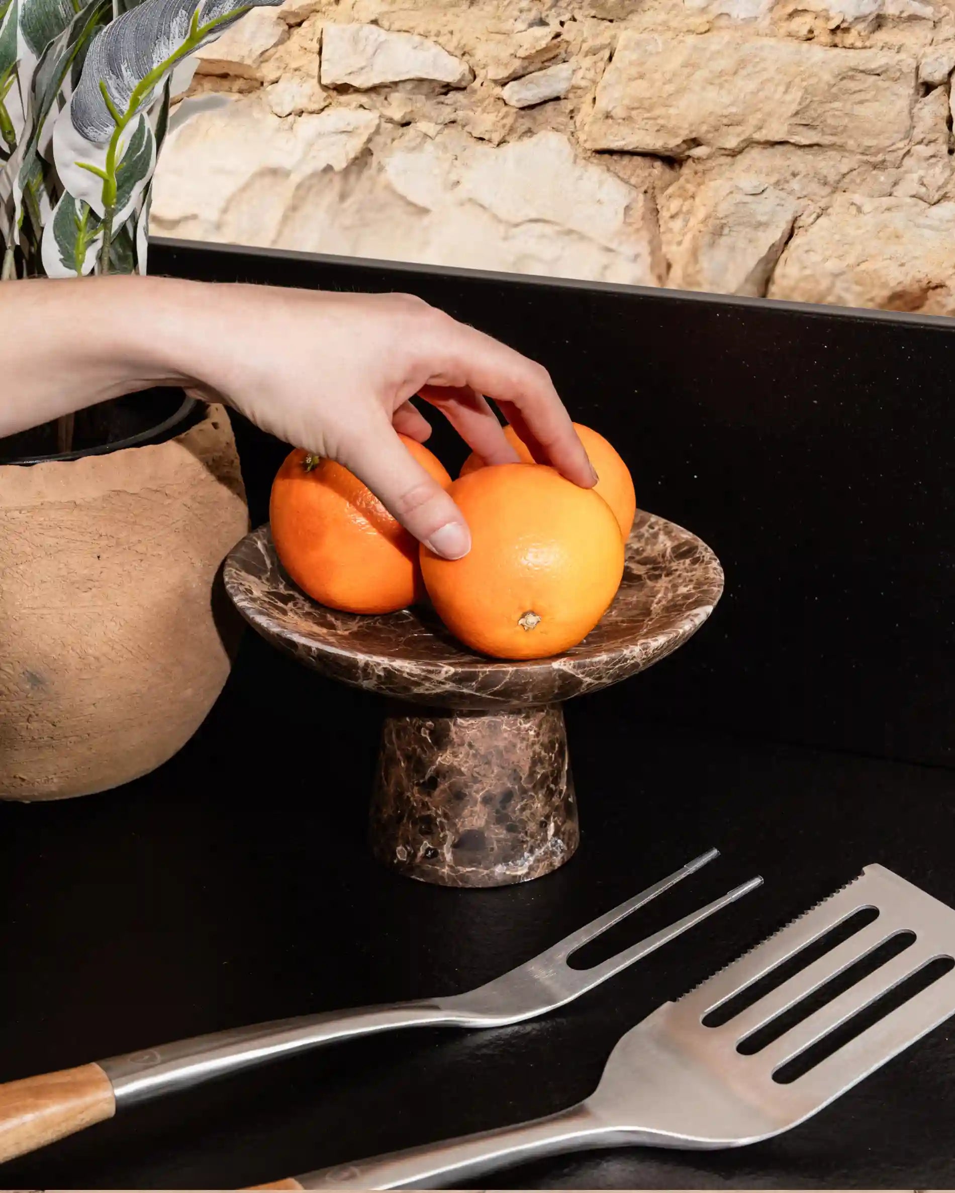 Hand picking oranges from a stone tray on Kokko black outdoor kitchen